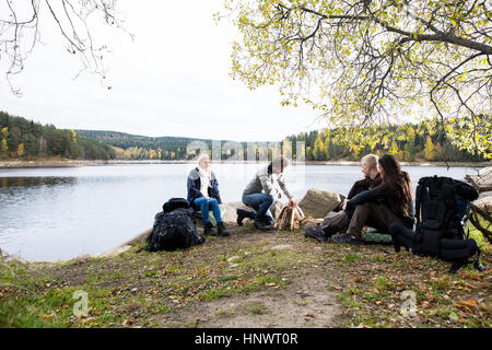 Friends Looking At Man Preparing Bonfire On Lakeside Camping Stock Photo