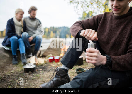 Man Grinding Coffee With Friends At Campsite Stock Photo