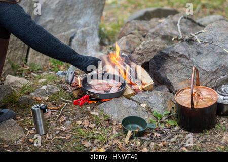 Woman Cooking Food Over Bonfire At Campsite Stock Photo