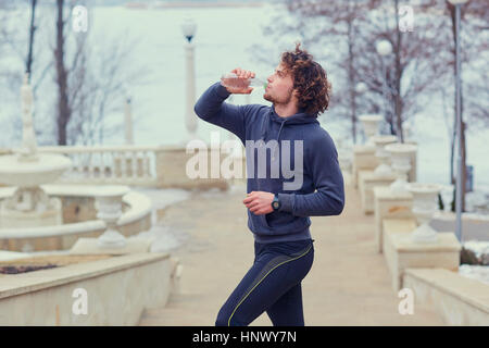 Curly Male runner drinks water from a bottle in park on the stai Stock Photo