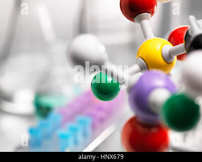 A molecular model of a chemical formula with laboratory equipment in the background Stock Photo