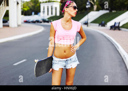 Portrait of young woman standing in street, holding skateboard Stock Photo