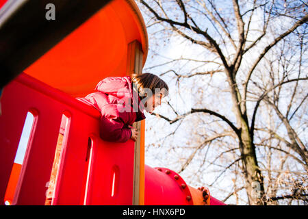 Boy looking out from top of red playground slide Stock Photo