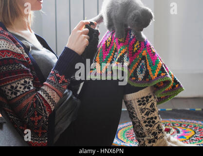 Woman sitting on floor crocheting with kitten balancing on her knee Stock Photo