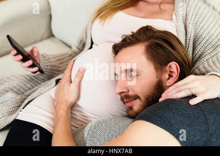 Man listening and touching girlfriend's pregnant stomach on sofa Stock Photo