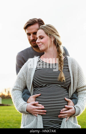 Man hugging and touching girlfriend's pregnant stomach in field landscape Stock Photo