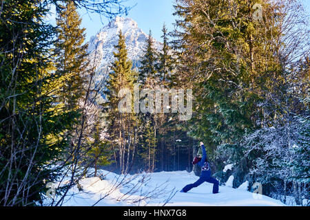 Woman in winter clothes practicing warrior yoga pose in snowy forest, Austria Stock Photo