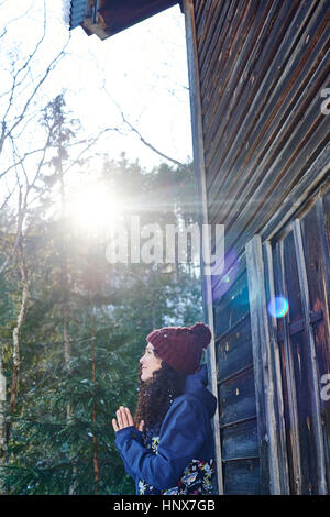 Woman in knit hat practicing yoga, meditating by log cabin Stock Photo