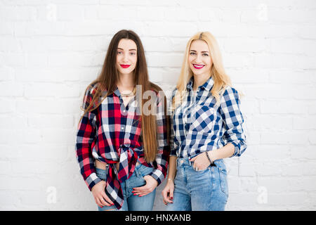 Female friends in checkered shirts and jeans standing together on the white wall background Stock Photo