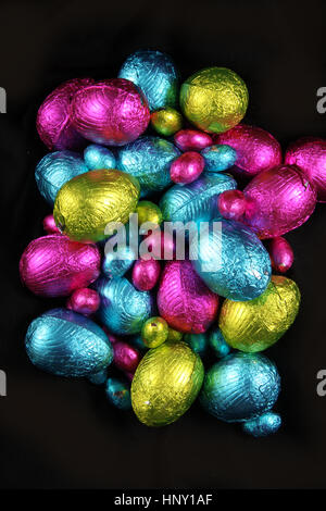 Pile of foil wrapped chocolate easter eggs in pink, blue & lime green. Stock Photo