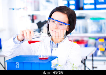 Attractive young female scientist working in laboratory.  Woman scientist looking at a red test tube in a lab Stock Photo