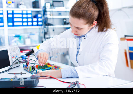 Engineer working with circuits. A woman engineer solders circuits sitting at a table.  Microchip production factory. Technological process. Assembling Stock Photo