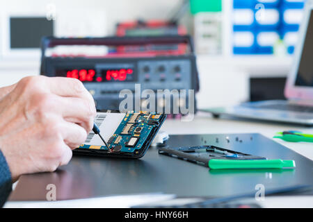 Closeup of hand of man sitting near computer and repairing cell phone Stock Photo