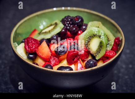 A green bowl of mixed fruit salad with blueberry kiwi tangerine and mango slices Stock Photo