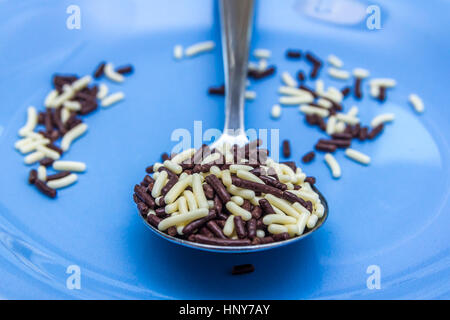 pure and white chocolate hagelslag sprinkles in spoon with blue background Stock Photo