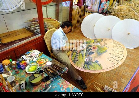 KAOHSIUNG, TAIWAN -- JULY 24, 2016: A male artist paints oil-paper umbrellas, which is a traditional art and craft product by the Chinese Hakka people Stock Photo