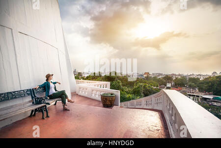 Woman tourist in hat sitting on the bench near temple Wat Saket also known as Golden Mount with view to Bangkok, Thailand Stock Photo