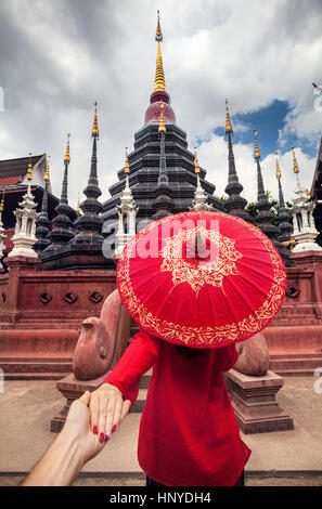 Woman with red traditional Thai umbrella holding man by hand and going to Black temple Wat Phan Tao in Chiang Mai, Thailand Stock Photo