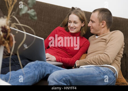Model release , Junges Paar sitzt mit Laptop auf der Couch - couple using laptop on couch Stock Photo