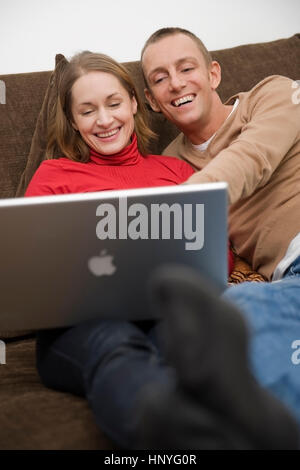 Model release , Junges Paar sitzt mit Laptop auf der Couch - couple using laptop on couch Stock Photo