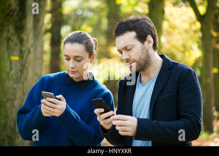 Couple checking smartphones while walking in woods Stock Photo