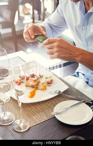 Man using smartphone to photograph his food in restaurant Stock Photo