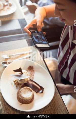Woman using smartphone to photograph gourmet dessert in restaurant Stock Photo