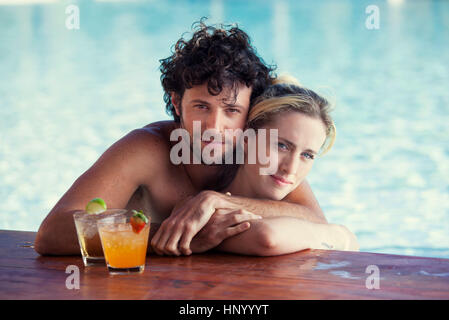 Couple relaxing together in pool with cocktails Stock Photo