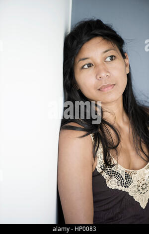 Woman leaning against wall, looking away in thought Stock Photo