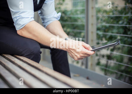 Man sitting on bench, using digital tablet, cropped Stock Photo