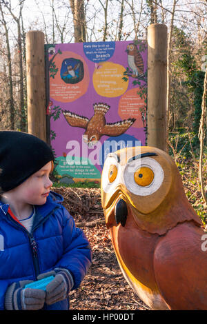 A young boy standing next to a wooden sculpture of 'Owl' (character from The Gruffalo) on the Gruffalo Trail, Horsenden Hill, Greenford, UK Stock Photo