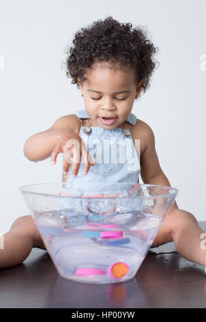Toddler girl playing with toys in bowl of water Stock Photo
