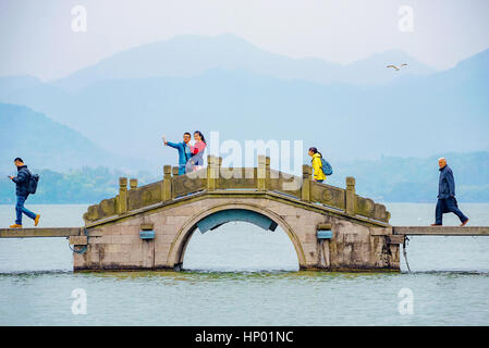 HANGZHOU, CHINA - MARCH 23: Chinese people walking along a bridge on the West Lake with a couple taking a self portrait on March 23, 2016 in Hangzhou. Stock Photo