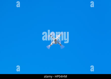 White quadcopter in blue sky, compact drone controlled by wireless remote, bottom view Stock Photo