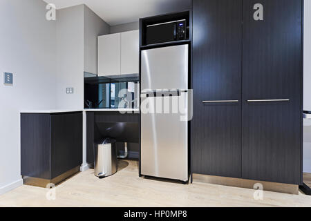 Modern stylish kitchenette corner in brand new apartment with fridge, cupboards, sink, tap and microwave oven. Stock Photo