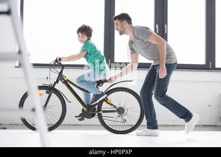 young father helping son to ride bicycle Stock Photo