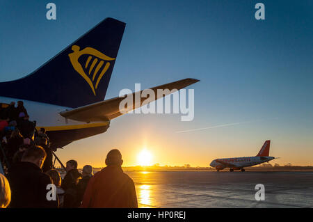 Passengers boarding a Ryanair Boeing 737-800 aircraft as an Easyjet Airbus taxis to runway at Bristol Airport, England, UK at sunrise Stock Photo