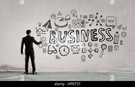 Back view of businessman drawing financial and business concepts on wall Stock Photo