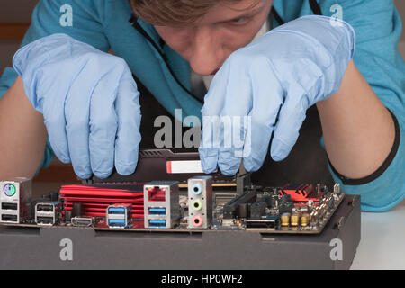 Young man with gloves  installing Ram DDR4 memory module in slot on motherboard.