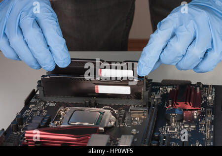 Close up of man hands with gloves installing Ram DDR4 memory module in slot on motherboard.