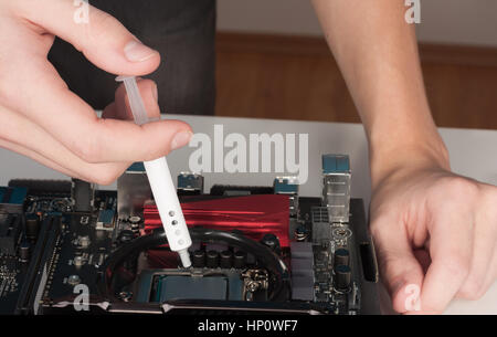 Close up of man hands with syringe applying thermal paste on the CPU processor on motherboard. Stock Photo