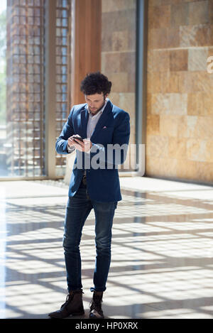 Man text messaging while walking through lobby Stock Photo