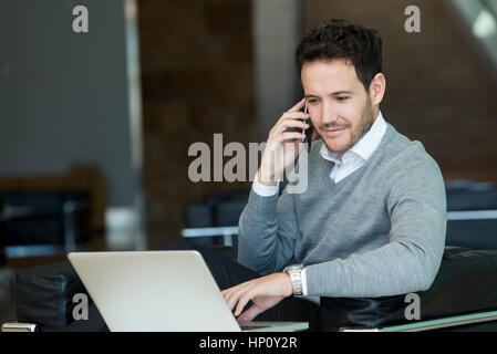 Businessman using cell phone and laptop computer at hotel lobby Stock Photo