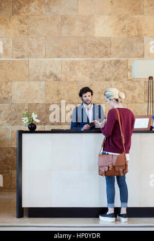 Woman text messaging during transaction with receptionist Stock Photo