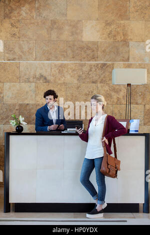 Woman looking at smartphone while waiting at reception desk Stock Photo