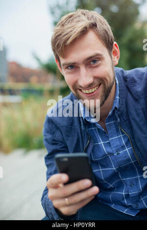Man using smartphone outdoors, smiling, portrait Stock Photo
