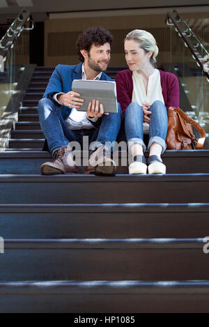 Couple sitting on steps, using digital tablet Stock Photo