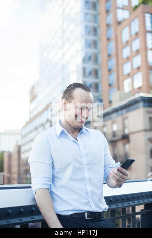 Man laughing while using smartphone outdoors Stock Photo