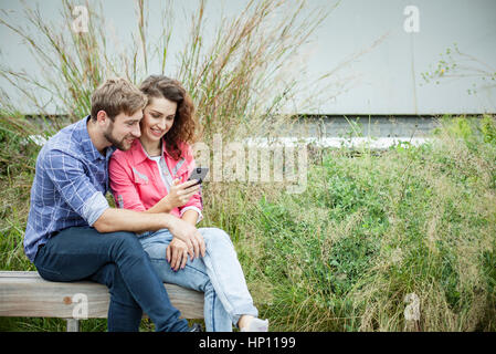 Couple sitting together on park bench, looking at smartphone Stock Photo