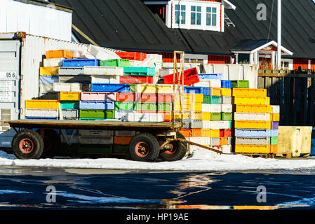 Nogersund, Sweden - February 14, 2017: Documentary of colorful fish crates stacked on wooden pallets in fishing port. Small trailer standing in front  Stock Photo